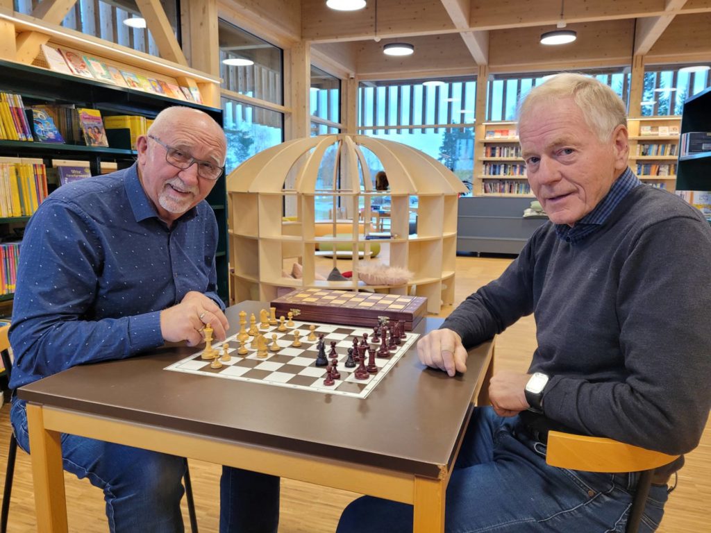LÆRER SJAKK: Arne Thobru i Våler pensjonistforening (til venstre) kunne heller ikke sjakk for Willy Fengsrud forklarte hvordan brikkene flyttes. Nå håper de to at flere eldre vil lære å spille.