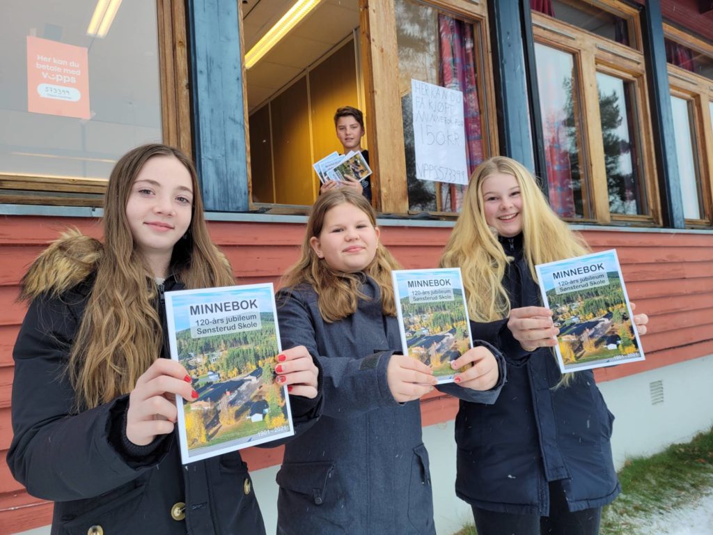 SELGES HERFRA: Fra et vindu selges minneboka fra Sønsterud skole mandag 13. desember. Aleksandra Siemaszko (fra venstre), Linnea Persby Framås og Elsa Lilly Johansson Skramstad håper mange kjøper. I luka for anledningen står Petter Haraldsen Glorvigen. Alle 7.-klasseelever ved Sønsterud skole.