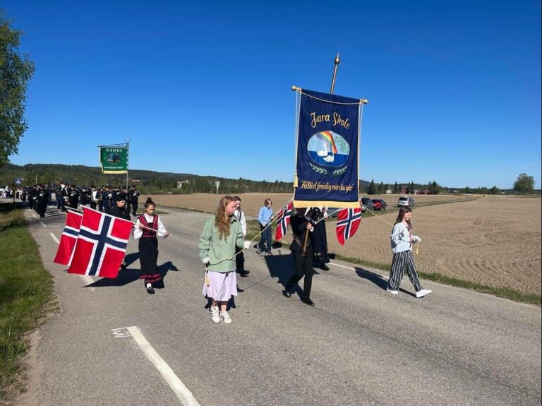 SKOLE OG KORPS: Fanen til Jara skole kom som vanlig først i barnetoget i Hof, før Åsnes Hornmusikk marsjerte bak og spilte kjente marsjer på nasjonaldagen. Været var det ingenting å si på.